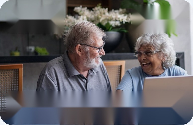 Older couple laughing together at a laptop